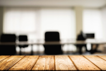 Empty wooden desk space over blurred office or meeting room background. Product display.