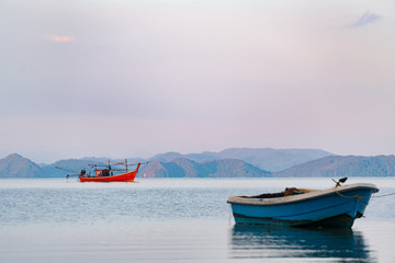 Obraz premium Long tail boat and fisherman in a sea bay with calm water on a background of mountains at sunrise in summer
