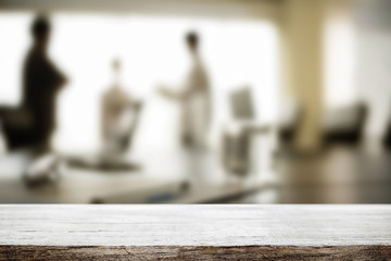 Empty wooden desk space over blurred office or meeting room background. Product display.