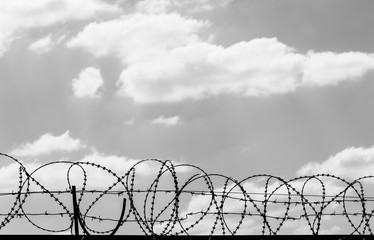 Black coiled barbed wire fence and sky with sunlit clouds
