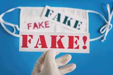 FAKE. Hand in medical rubber gloves holds an inscription on a blue background with a white respiratory mask. Concept of Coronavirus fake hoax covid-19 sars-cov-2 alert for hoax fake news.