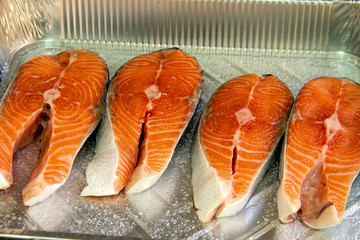 Four fresh raw salmon on a foil and salt baking dish close up.