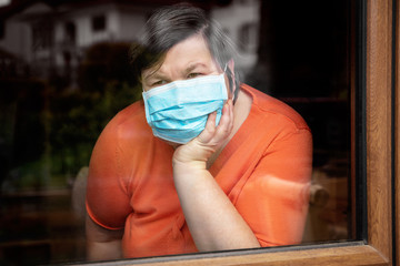 Mentally disabled woman with surgical mask looking out at window, coronavirus