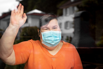 Mentally disabled woman with surgical mask waving out at a window, covid-19