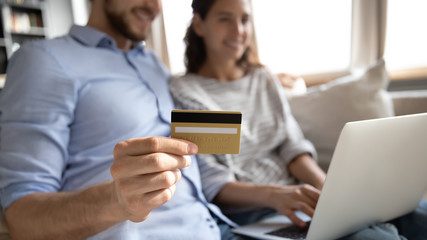 Close up focus of young couple use credit card shopping online on laptop from home, excited man and woman make payment with internet banking service system on modern computer, ecommerce concept