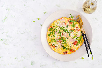 Omelette with tomatoes, ham, cheese and green herbs on plate.  Frittata - italian omelet. Top view, overhead, copy space