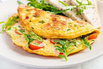 Omelette with tomatoes, ham, cheese and green herbs on plate.  Frittata - italian omelet.