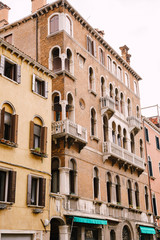 Fototapeta na wymiar Closeup of the facade of a building, on the streets of Venice, Italy. Five-story stone building with white balconies with columns, classic Venetian arched windows.