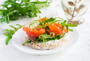 Open sandwich with  crispbread salted salmon, cream cheese, sliced cucumber and arugula on plate.