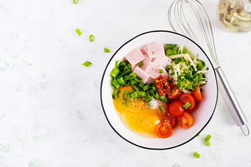 Omelette ingredients: eggs, ham, tomatoes, green herbs, milk and cheese on the light table. Top view, overhead, flat lay