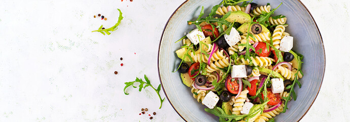 Pasta salad with tomato, avocado, black olives, red onions and cheese feta. Mediterranean cuisine. Top view, overhead, banner