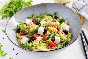 Pasta salad with tomato, avocado, black olives, red onions and cheese feta. Mediterranean cuisine.