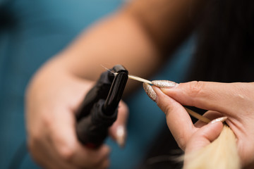 Preparing a strand of hair for extension. Hair and hair tools close-up.