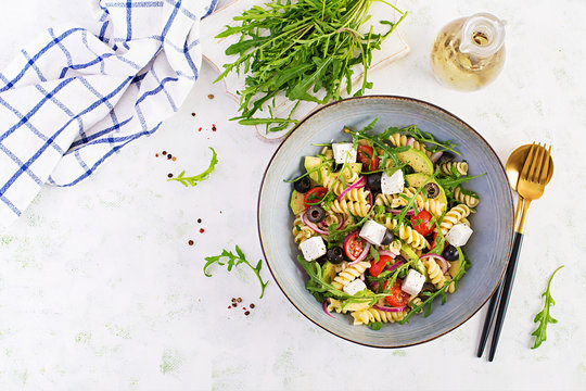 Pasta salad with tomato, avocado, black olives, red onions and cheese feta. Mediterranean cuisine. Top view, overhead, flat lay
