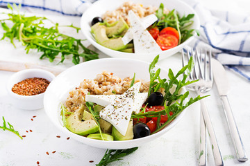Breakfast oatmeal porridge with greek salad of tomatoes, avocado, black olives and arugula. Healthy balanced food.