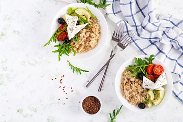 Breakfast oatmeal porridge with greek salad of tomatoes, avocado, black olives and arugula. Healthy balanced food. Top view, flat lay, copy space