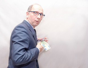 A man in glasses, a Caucasian, is hiding money in his pocket. Man is afraid of surprise