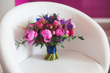A wedding bouquet of pink peonies and hydrangeas stands on a white sofa. the bouquet is tied with a blue ribbon