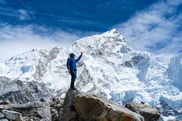 A male solo trekker standing on a rock at Everest Base Camp in Nepal and enjoying the close-up view of Nuptse Mountain (7861 m / 25791 ft.) in the background on a clear sunny day.