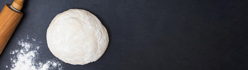 Dough, rolling pin and flour on a black background