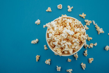 Popcorn in a bowl on blue background, top view.