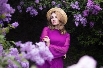 Young beautiful woman among the bushes of blossoming lilac