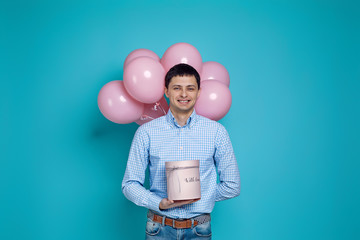 happy caucasian man holding gift box and pastel pink air balloons isolated on blue background. birthday party.