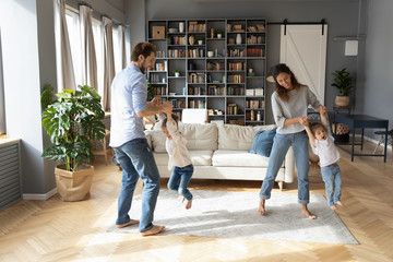 Overjoyed young family with little preschooler daughters have fun playing together in living room,...