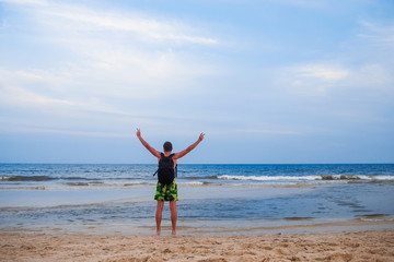 man with a backpack stands back with hands up background the ocean