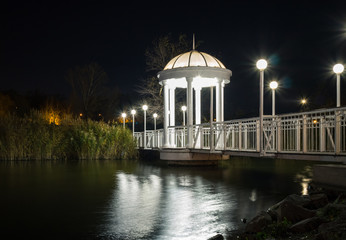 Bridge across the pond in the park with gazebo and lampposts at night