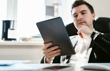 Young successful businessman and office employee reading news on his tablet. Coffee break during the working day. A financial analyst or broker studies stock market fluctuations. Economic crisis 2020.
