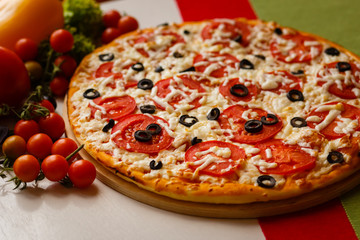 Hot italian pizza on a table with vegetables