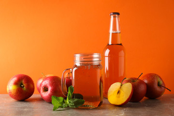 Composition with cider and apples on gray table against orange background