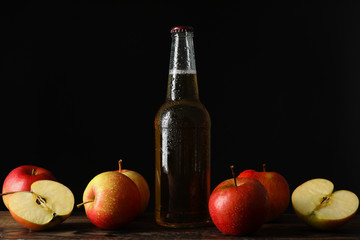 Composition with cider and apples on wooden table against black background