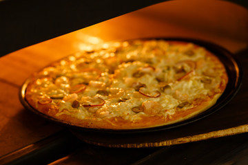 Baking a pizza in oven. Hot pizza in a dish on a shovel in a furnace.