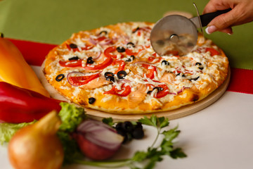 Slicing hot pizza by cutter knife.