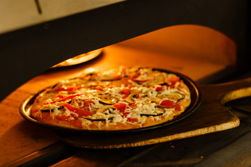 Baking a pizza in oven. Hot pizza in a dish on a shovel in a furnace.