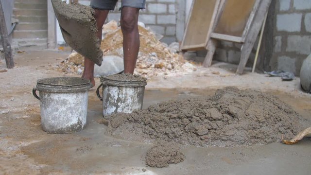 local guy gathers grey wet cement into basket on construction territory slow motion close view. Concept slavery and poverty