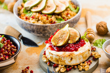 close-up view of tasty healthy dish with fruits, nuts, honey, camembert cheese, couscous and pomegranate seeds on wooden table