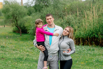 Obraz premium Sports family - mom, dad and daughter 5 years old in sportswear are hugging for a walk in the park