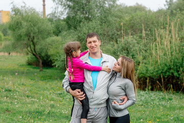 Obraz premium Sports family - mom, dad and daughter 5 years old in sportswear are hugging for a walk in the park