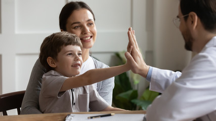 Little boy patient give high five have fun at consultation visit at pediatrician with mom, male doctor greeting cheer small child client at clinic checkup or examination, children healthcare concept