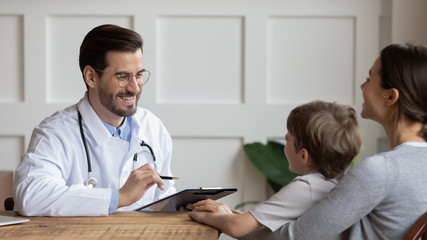 Smiling male doctor talk consult write in medical card at consultation with little boy patient in hospital, mother with small son visit do checkup at pediatrician, medicine, healthcare concept - obrazy, fototapety, plakaty
