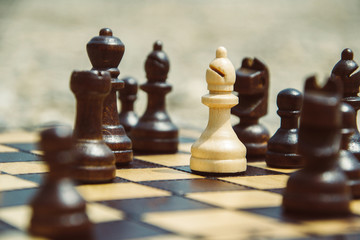Bishop chess piece standing on a chessboard. Surrounded by black figures. Racism concept. Playing chess outdoors. 