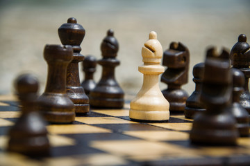 Bishop chess piece standing on a chessboard. Surrounded by black figures. Racism concept. Playing chess outdoors. 