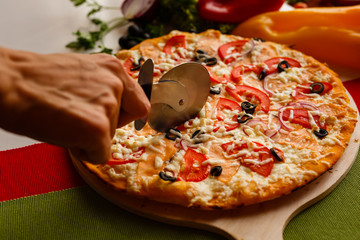 Cutting a pizza to a slices by cutter. Close-up photo