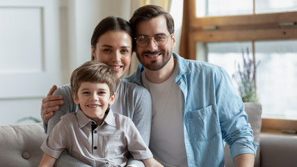 Portrait of smiling young family with little preschooler son sit relax on couch in living room, happy Caucasian parents with small boy child rest in cozy home, enjoy weekend together, bonding concept