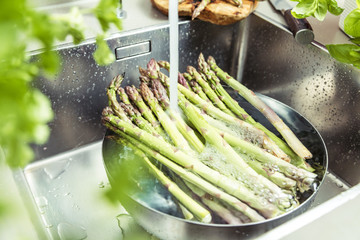 cropped shot of male hands in soil washing fresh asparagus in kitchen sink.