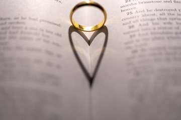 A wedding Ring on the bible with shadow of heart shape on the page