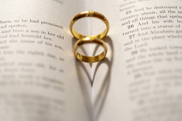 Two wedding Ring on the bible with shadow of heart shape on the page